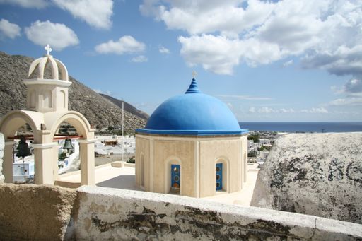 The blue-domed church under the sunlight and a blue cloudy sky in Santorini, Greece