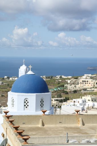 A vertical shot of the blue-domed church in Santorini surrounded by buildings and the sea at daytime in Greece