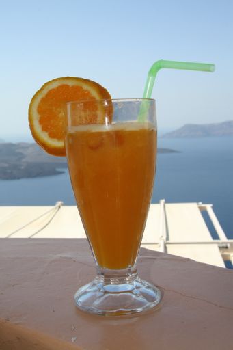 A vertical shot of a glass fresh orange juice with a plastic straw under the sunlight in Greece