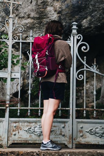 A vertical shot of a person with a backpack standing behind a metallic door with their hands crossed