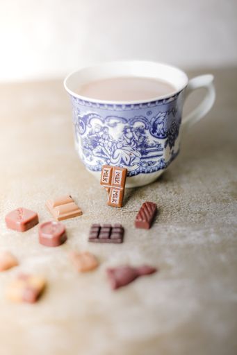 A closeup shot of a ceramic Latte drink next to chocolate pieces on a beige surface