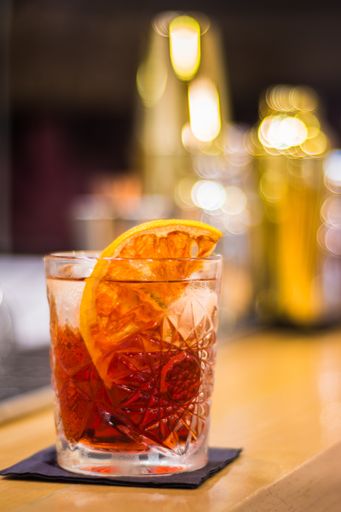 A vertical closeup shot of a Negroni cocktail with a lemon on a bar stand background