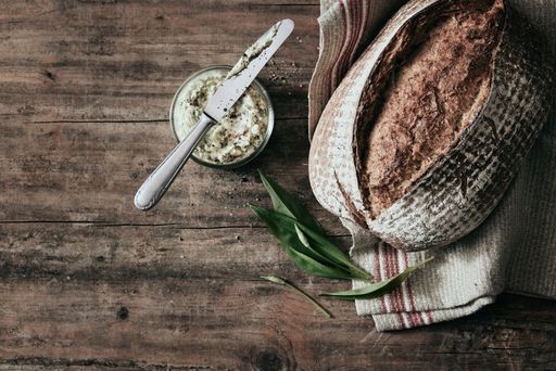 A top view of a freshly baked loaf of bread with a jar of lard and towel on the wooden board