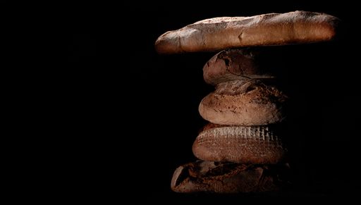 Delicious freshly baked bread loaves and baguettes stacked on top of each other on a black background