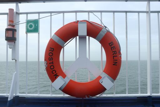 A Close up shot of a ring life jacket on a ship with text "Berlin Rostock" and sea in the background