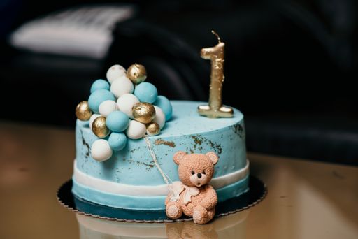A blue birthday cake with a golden, number one candle, decorated with a little bear and balls