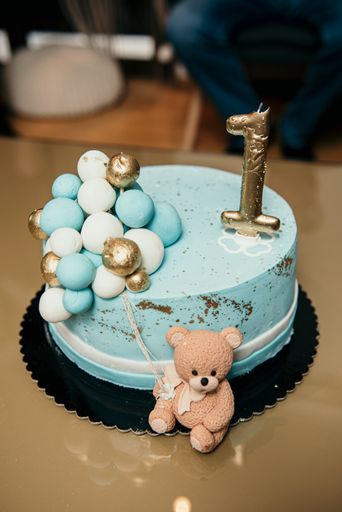 A vertical shot of a blue birthday cake with a number one candle and a little bear on the side