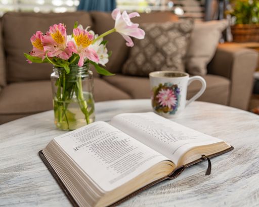 A horizontal shot of a book set on a coffee table with a mug and flowers on a brown couch background