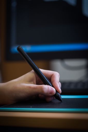 A vertical shot of a hand drawing on a graphic design tablet with a black pen