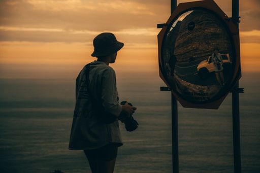 A man holding a camera standing in front of a mirror near the sea during sunset