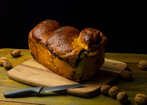 A freshly baked loaf of bread rests on a wooden cutting board, partnered with a variety of nuts on the side