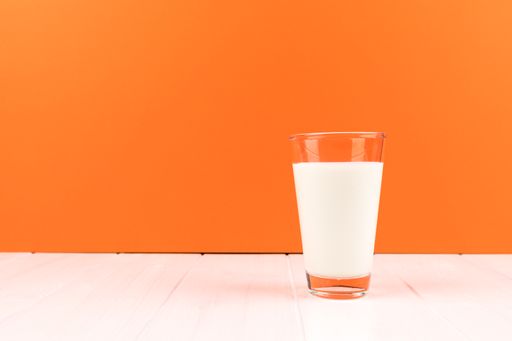 A closeup minimalistic shot of a glass of milk with an orange and white background