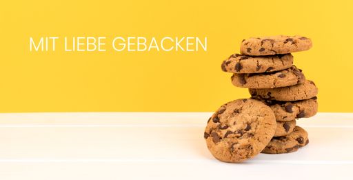 A stack of cookies on a white table with German text mit liebe gebacken, which means baked with love on a yellow background with copy space