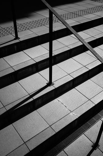 A vertical grayscale shot of modern stairs in a street with a metal railing