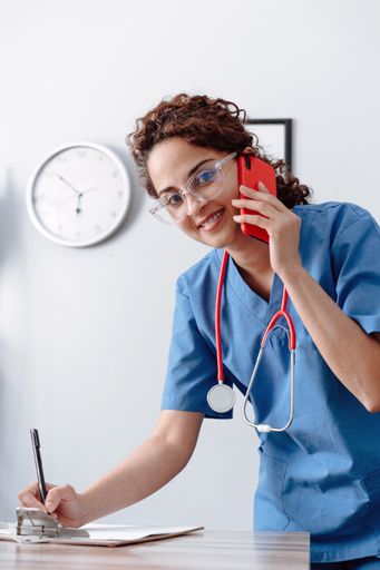 A young happy female doctor writing on a piece of paper while talking on the phone