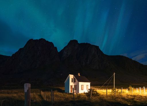A horizontal shot of a white house with a black rooftop surrounded by high rocky mountains under the starry sky