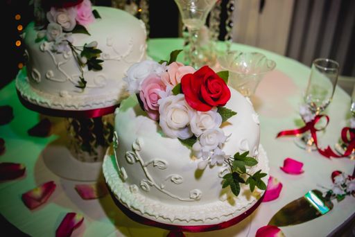 A  horizontal shot of two small wedding cakes decorated with red, pink and white flowers set on a white table