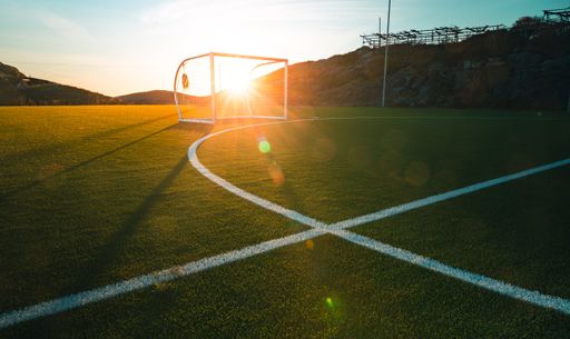 A wide shot of a football pitch with the sun rays under the beautiful cloudy sky
