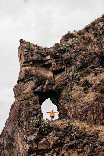 A vertical shot of  man in a yellow jacket enjoys nature standing on a rock