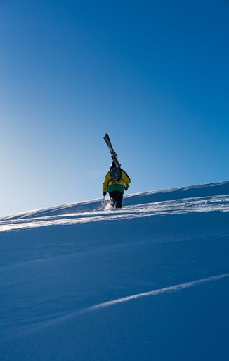 A vertical shot of a male with a yellow coat walking in the snow  carrying a skiing board
