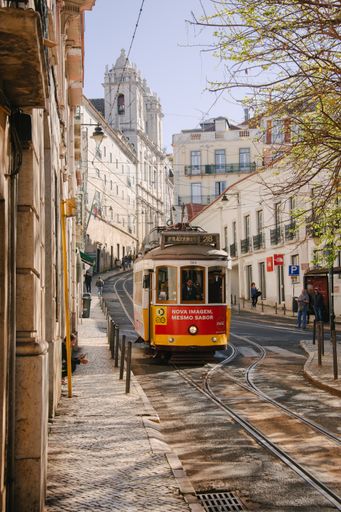 A vertical shot of a red and yellow Tram  passing through Lisbon city in Portugal