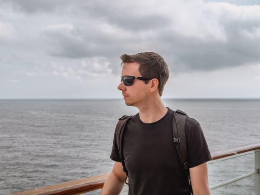 A closeup of a man on a cruise ship with the ocean in the background