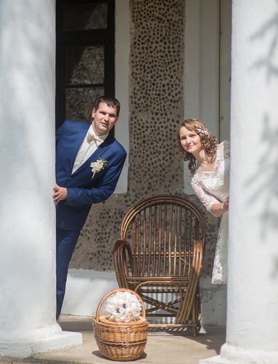 A vertical shot of a beautiful couple hiding behind the walls -a wedding photography