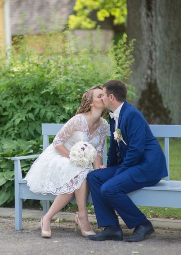 A vertical shot of newlyweds sitting on a bench in the park and kissing