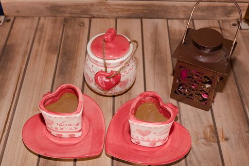 A high angle closeup shot of heart-shaped ceramic coffee mugs and a jar next to a wooden lantern full of rose petals on a wooden table