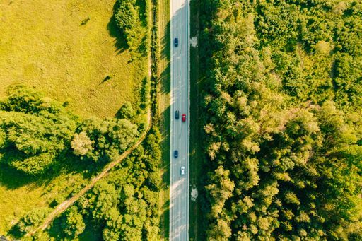 An aerial shot of cars on a highway during daytime with a green field and a forest from right and left