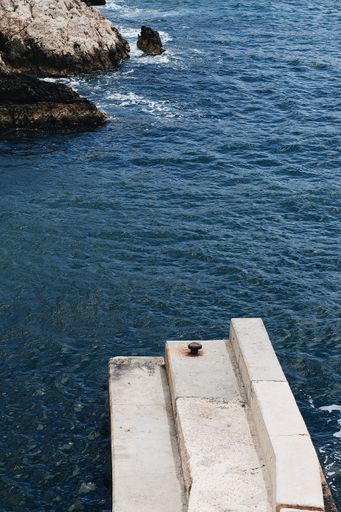 A vertical shot of an azure sea with some small rocks and an artificial stone dock on a side