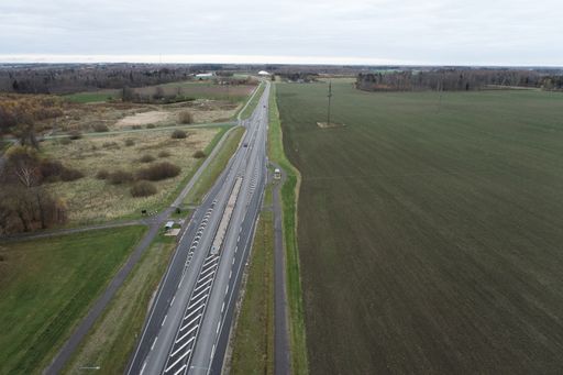 A drone view of highway road with big farms on its sides under cloudy sky