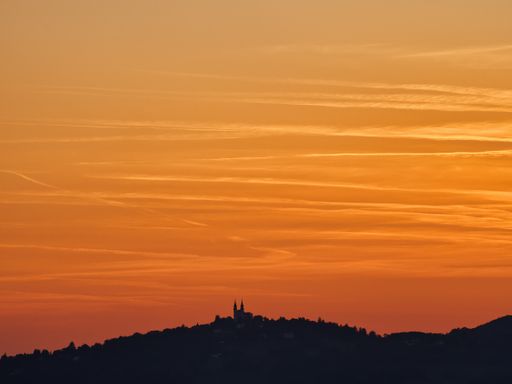 Silhouette of a church from a distance with an orange cloudy sky photographed backlit in evening sun, in Linz Austria, Poestlingberg church