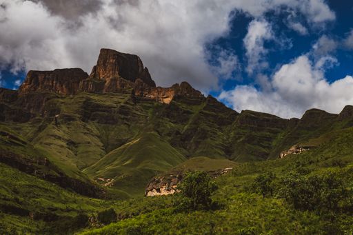 A scenic view of a rocky mountain range covered with green trees and plants under a blue cloudy sky