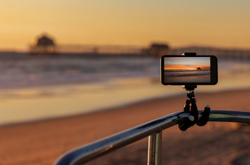 A selective focus of a phone on a tripod shooting the Huntington Beach, California at sunset