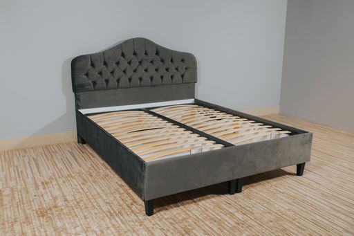 A bed with gray fabric upholstery and a wooden frame without mattress in an empty room