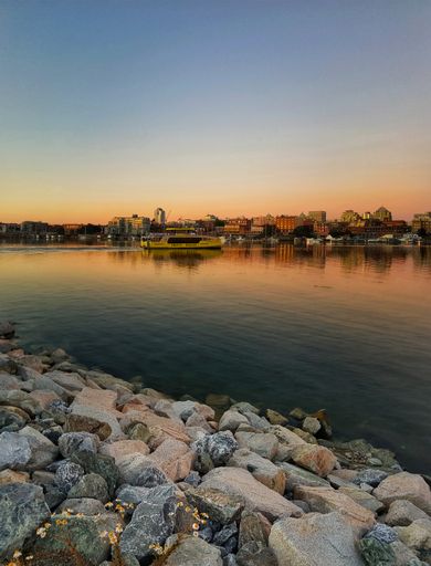 A vertical shot of a rocky bank of a river against downtown of Victoria, BC, Canada at sunset