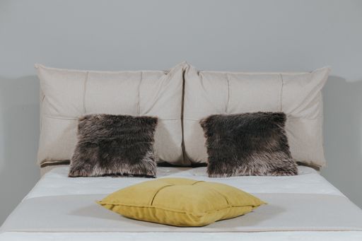 A closeup shot of a bed with beige fabric upholstery and stylish pillows