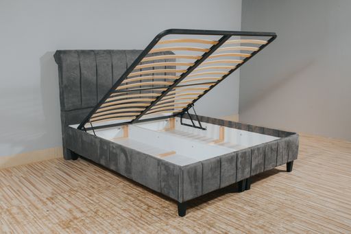 A gray bed with a storage space revealed by lifting the wooden slatted base