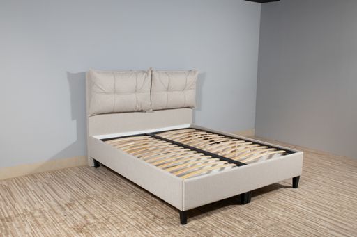 A bed with beige fabric upholstery and a wooden frame without mattress in an empty room
