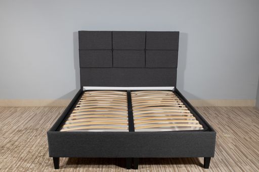 A bed with gray fabric upholstery and a wooden frame without mattress in an empty room