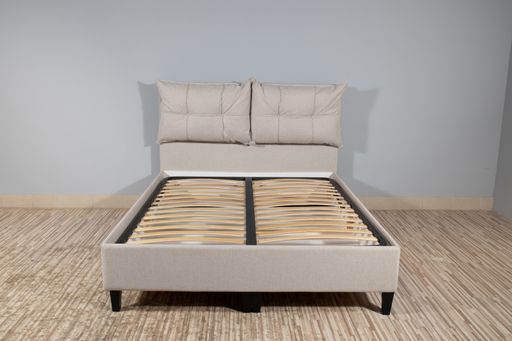 A bed with beige fabric upholstery and a wooden frame without mattress in an empty room