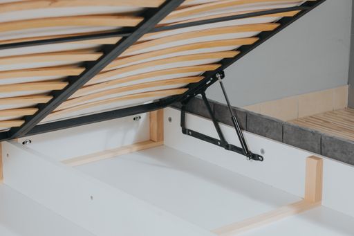 A closeup shot of a bed with wooden frame and lifting mechanism for a storage space