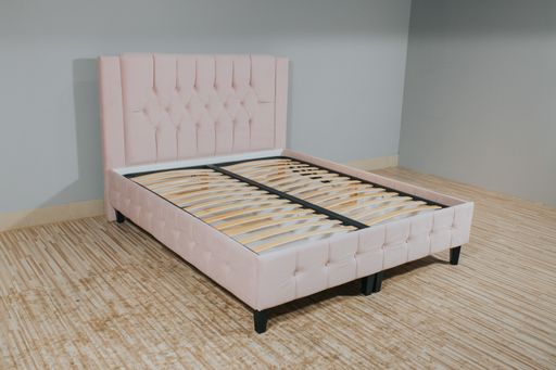 A bed with pink fabric upholstery and a wooden frame without mattress in an empty room