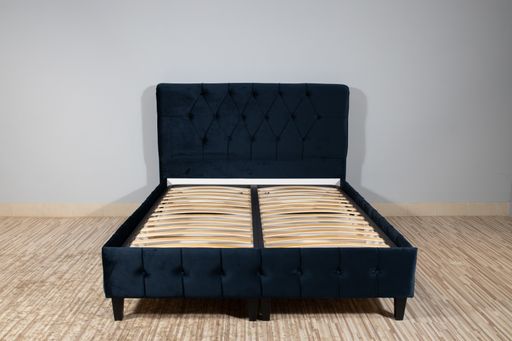 A bed with blue fabric upholstery and a wooden frame without mattress in an empty room