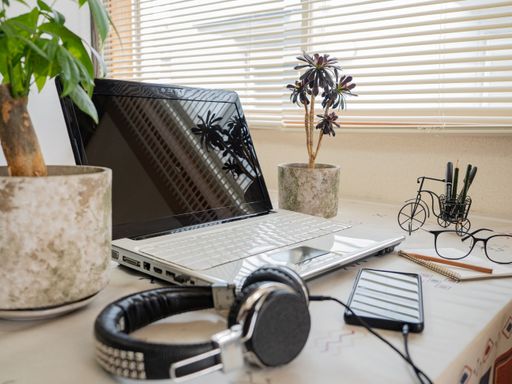 A selective focus shot of a laptop with headphones, a phone, a notebook, and table plants on a desk