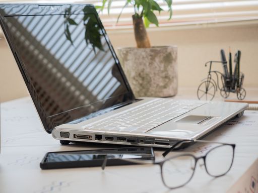A laptop on the table with a smartphone and eyeglasses