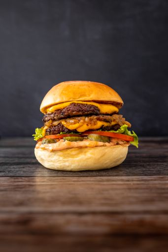 A vertical shot of a burger with bacon, fries, lettuce, melted cheese, crispy sweet onions and tomato