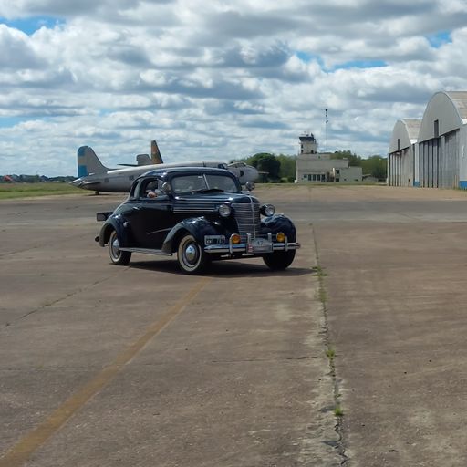 old black Chevrolet Chevy Master Deluxe coupe 1938 by GM in airstrip. Plane and hangars on the back. CADEAA 2022 at MNA classic car show. Copyspace.