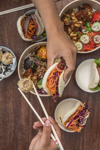 A top view shot of a table with Asian street food, poke bowl, bao, bun, chopsticks